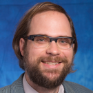 A professional headshot of Dr. Bradley Ander. He is a fair-skinned man with brown hair, glasses, a mustache, and beard.